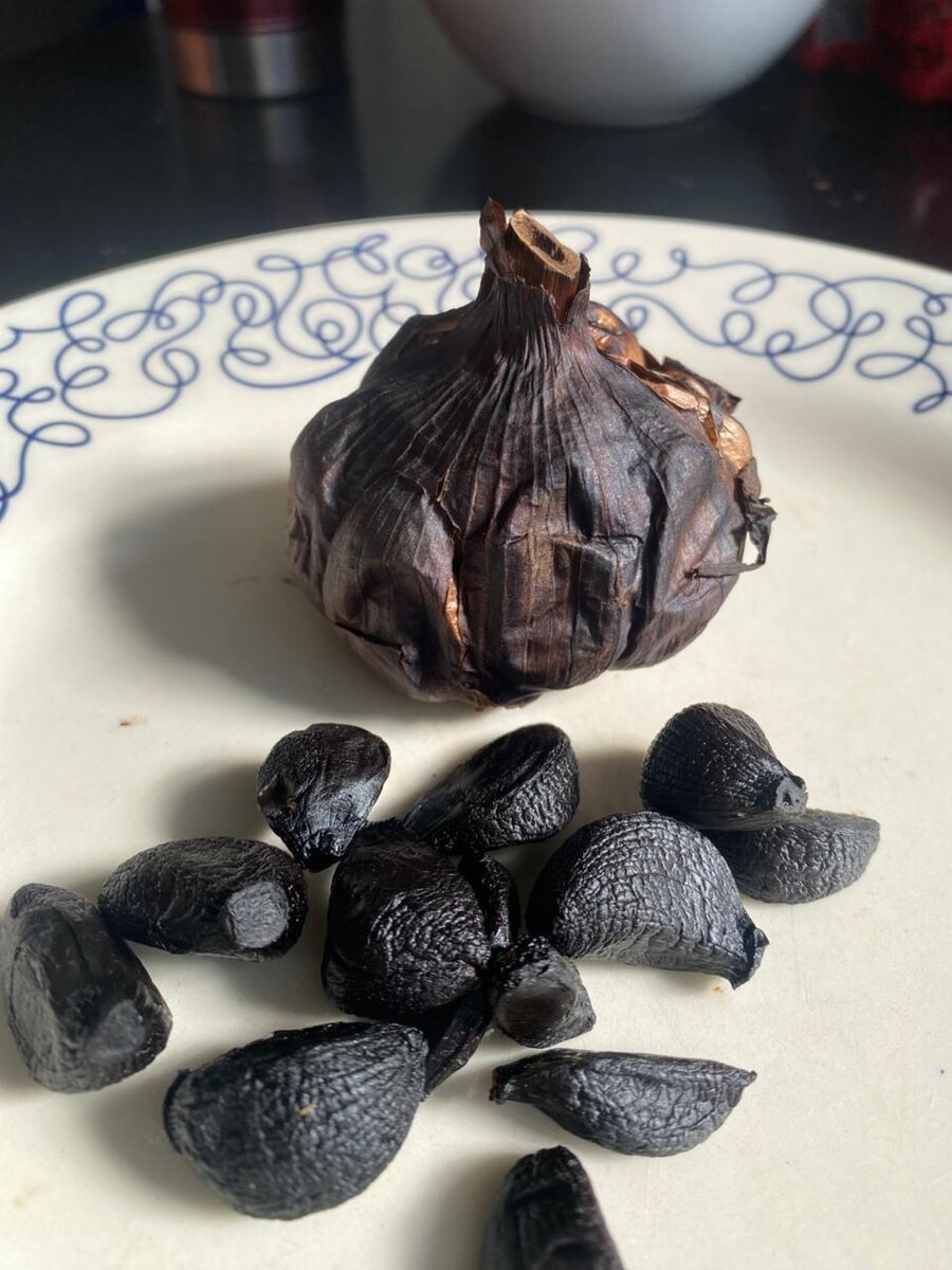 Bulbo de alho negro aberto, com os dentes pretos e brilhantes ao lado
