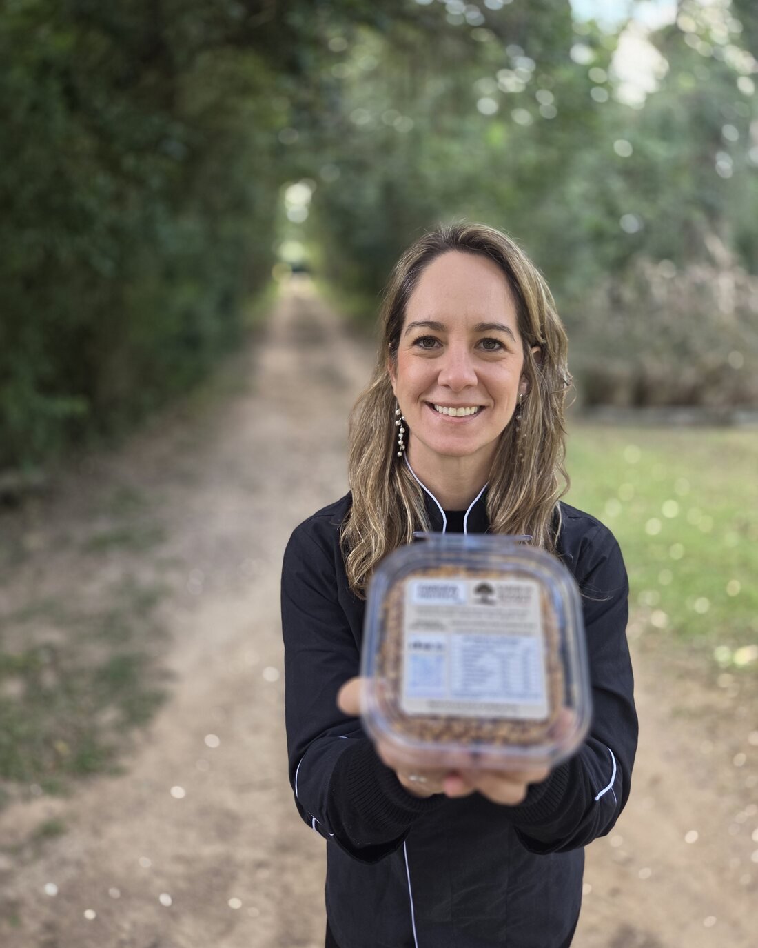A produtora da Sabor do Bosque segurando um pote de farofa proteica no mesmo caminho