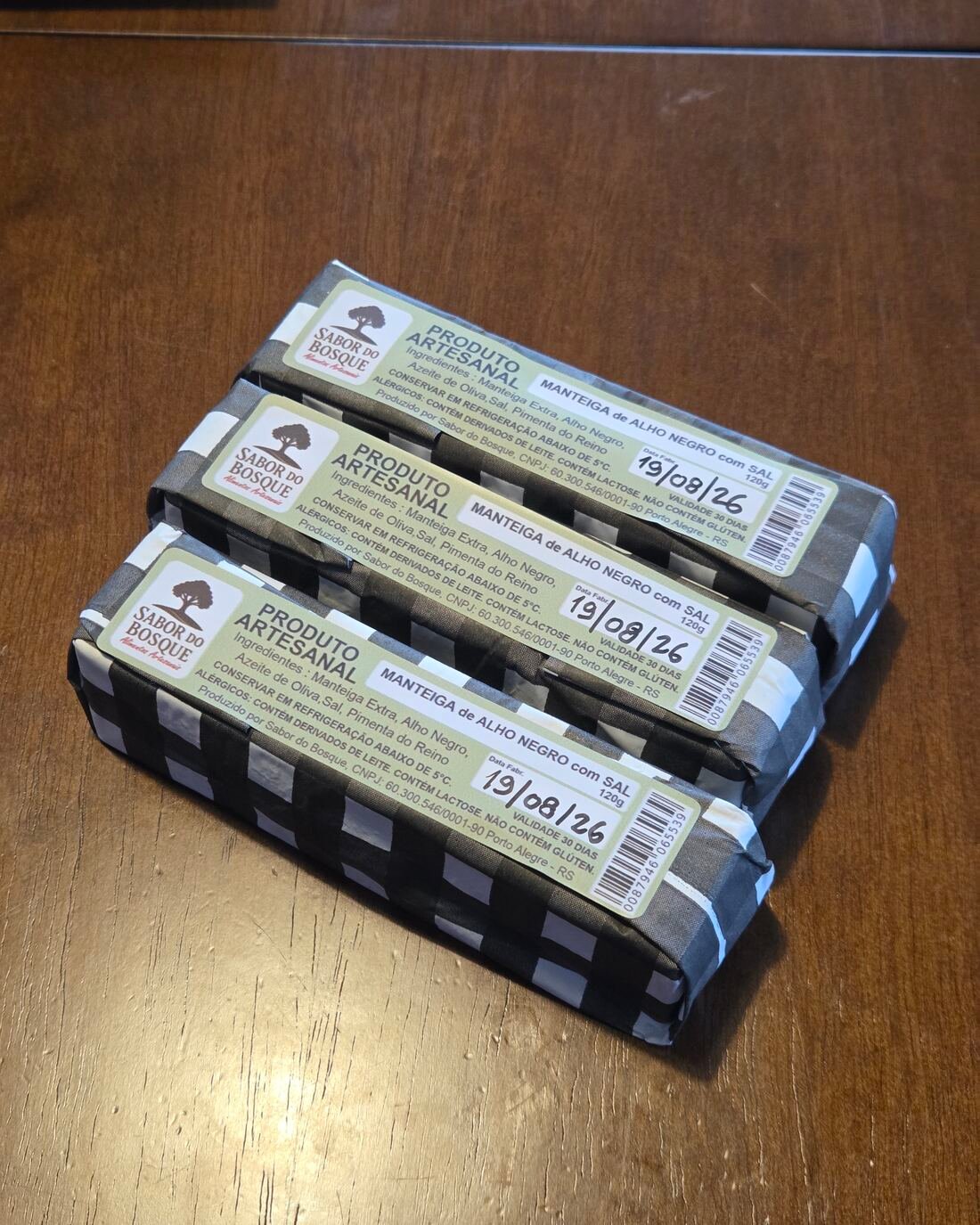 Três barras de manteiga de alho negro com sal, embrulhadas em papel xadrez preto e branco